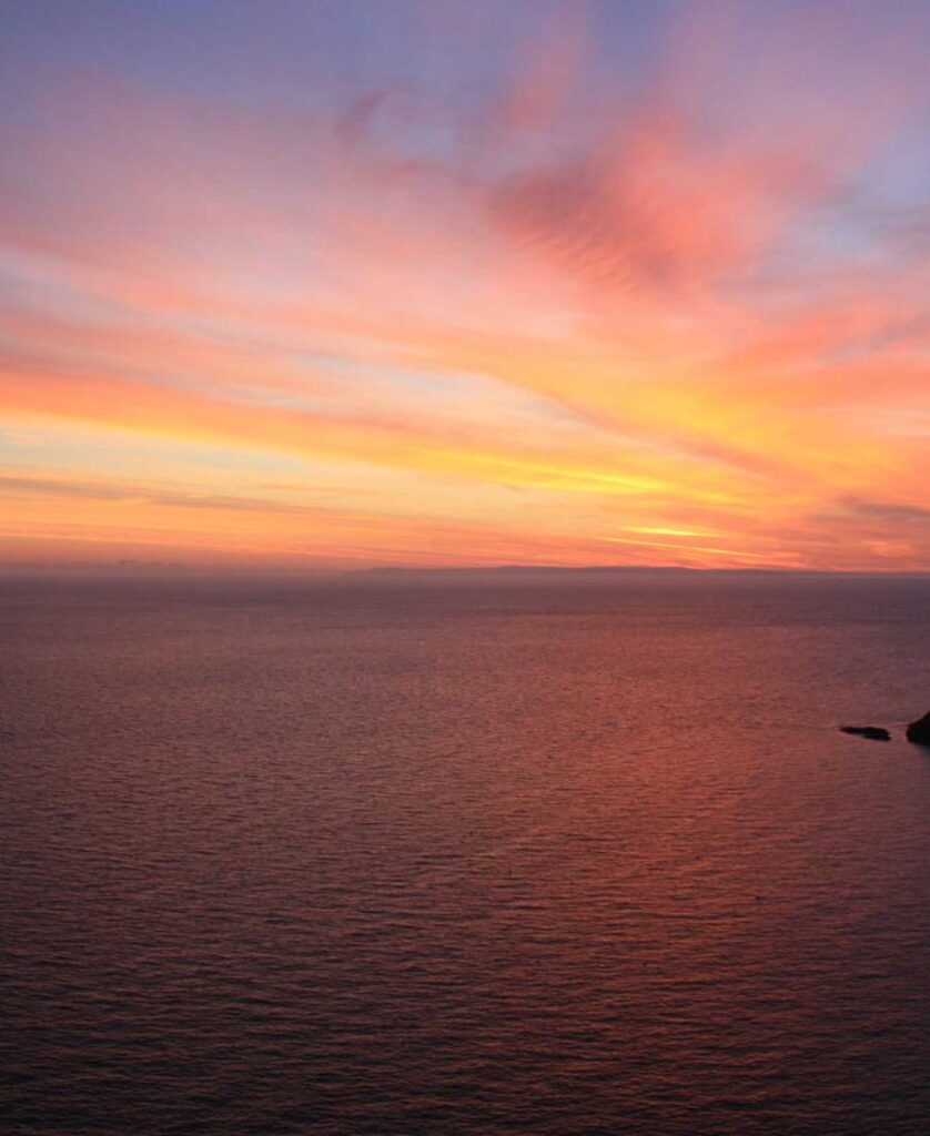 Coucher de soleil éclatant sur l'océan avec des reflets roses et orangés sur l'eau calme et sereine.
