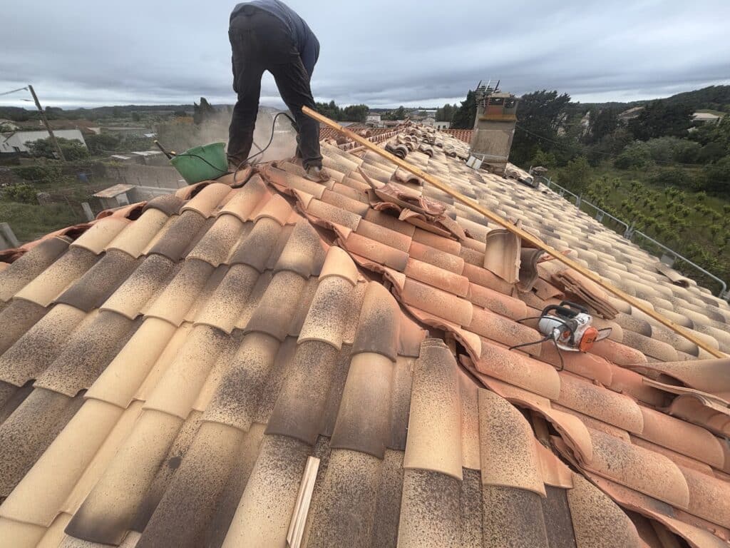 Rénovation Toiture : Travaux de Pose de Tuiles Romanes Artisan découpant des tuiles en terre cuite sur un toit en rénovation avec une scie circulaire.